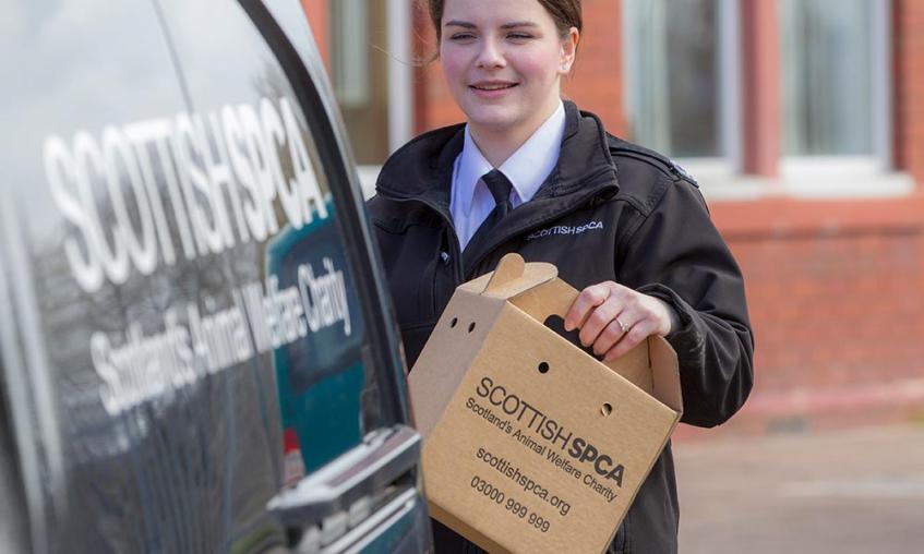 Member of staff behind an SSPCA van holding box 